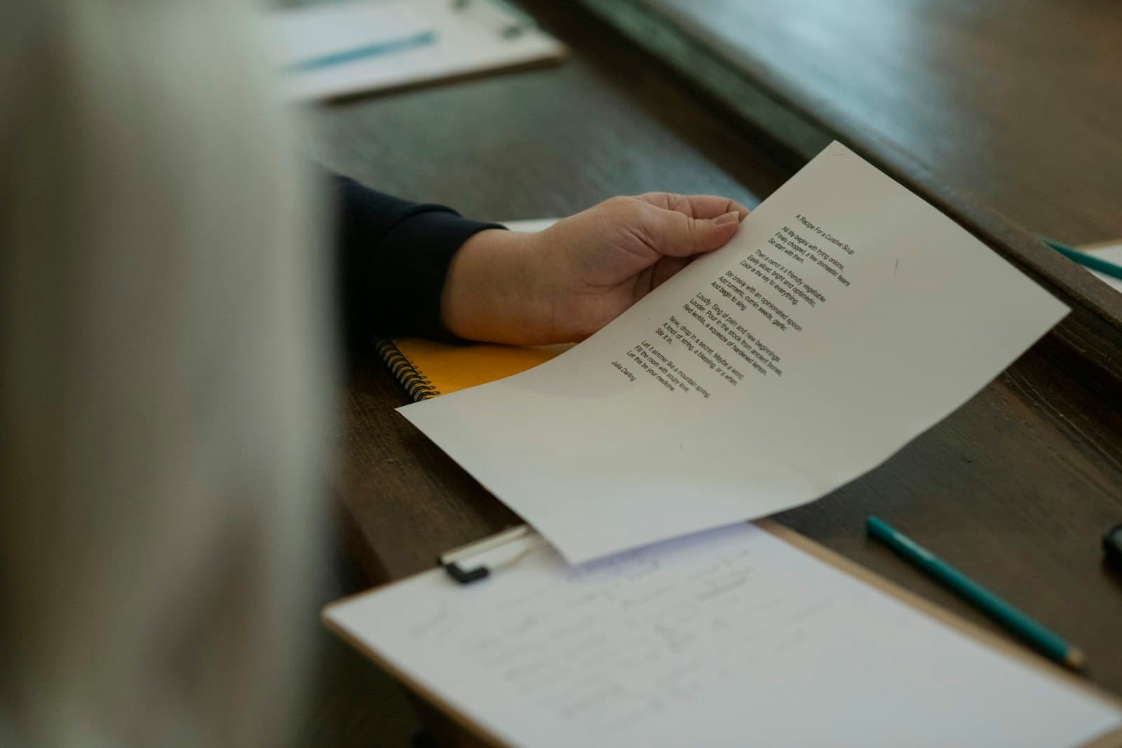 A hand holding a printed sheet of results at a table, angled toward the light to read it.